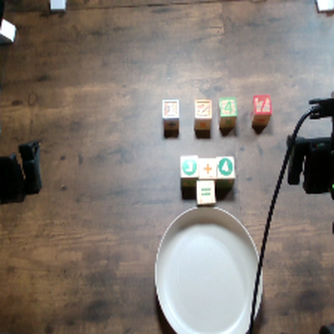 overhead view of the scene: blocks spelling 3 + 4 =, candidate blocks 1 2 4 7, empty plate